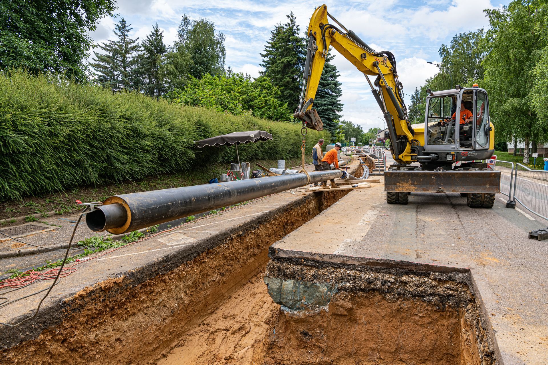 Travaux routiers avec une excavatrice à côté d'une tranchée et d'une grosse canalisation.