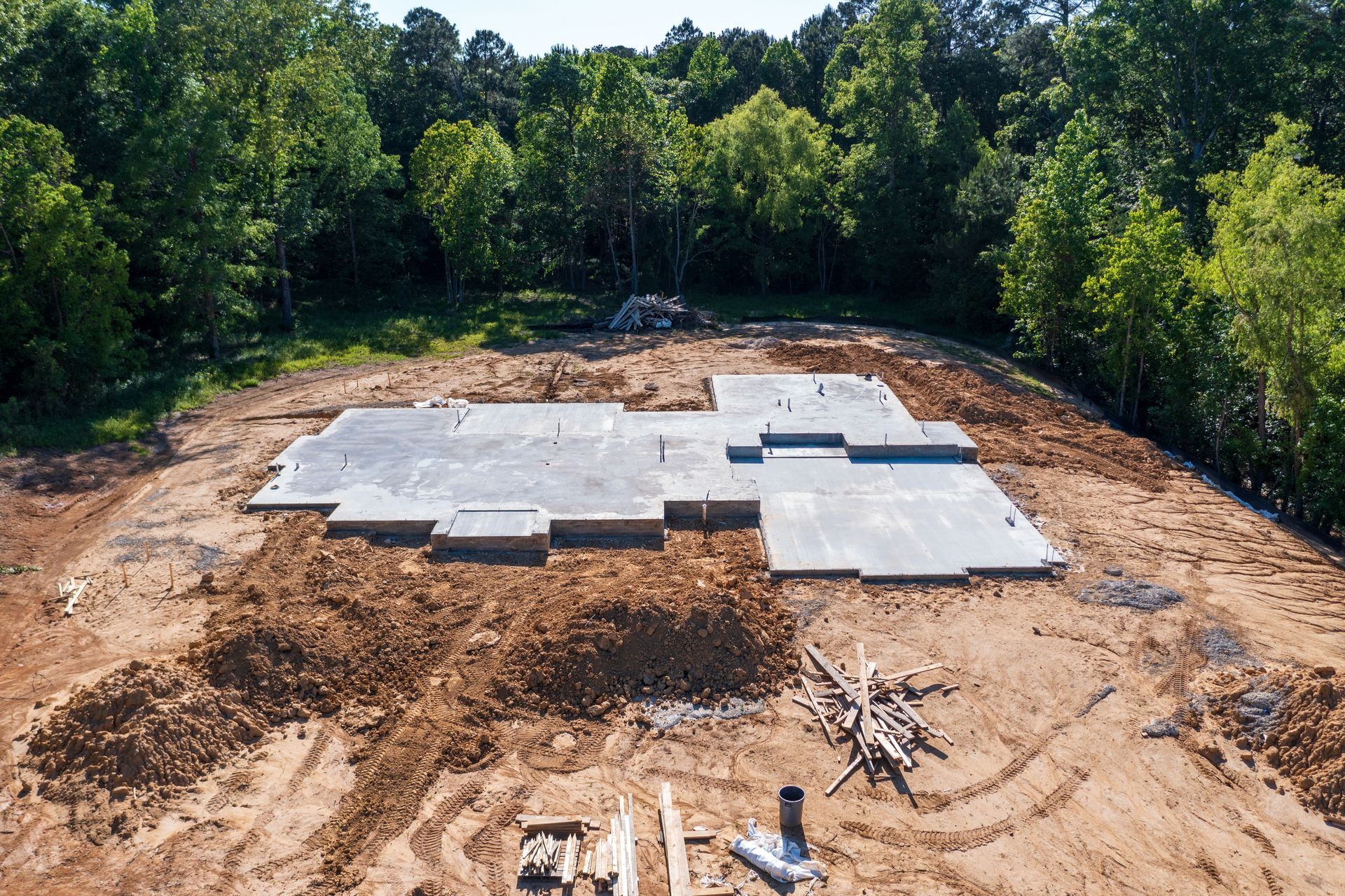 Dalles de fondation en construction sur un terrain entouré d'arbres.