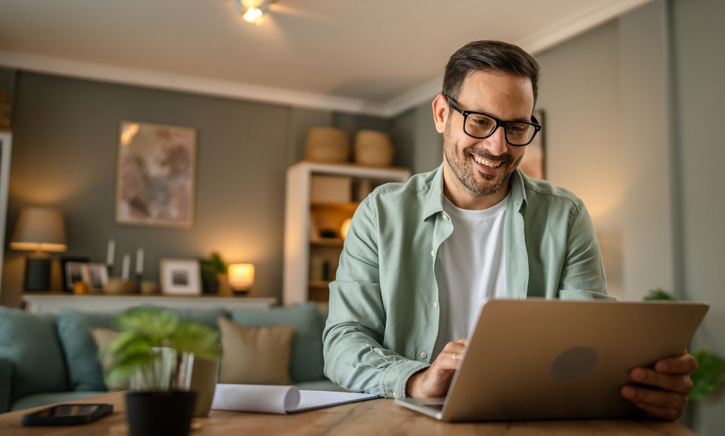 Un homme souriant, portant des lunettes, qui consulte son ordinateur.