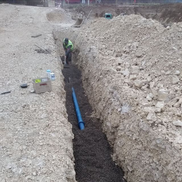 Un ouvrier creuse une tranchée à côté d'un tuyau bleu sur un chantier de construction.