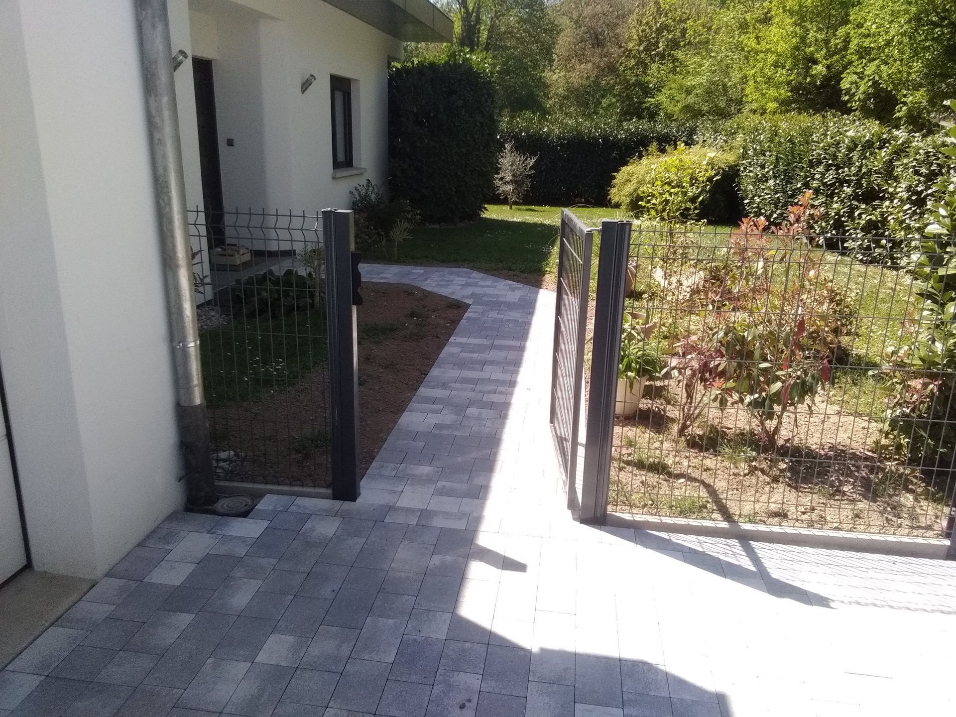 Un portillon ouvert qui donne accès à une allée pavée.