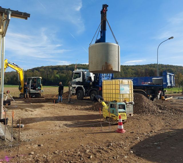 Chantier de construction avec une grue soulevant une cuve à eau en béton.