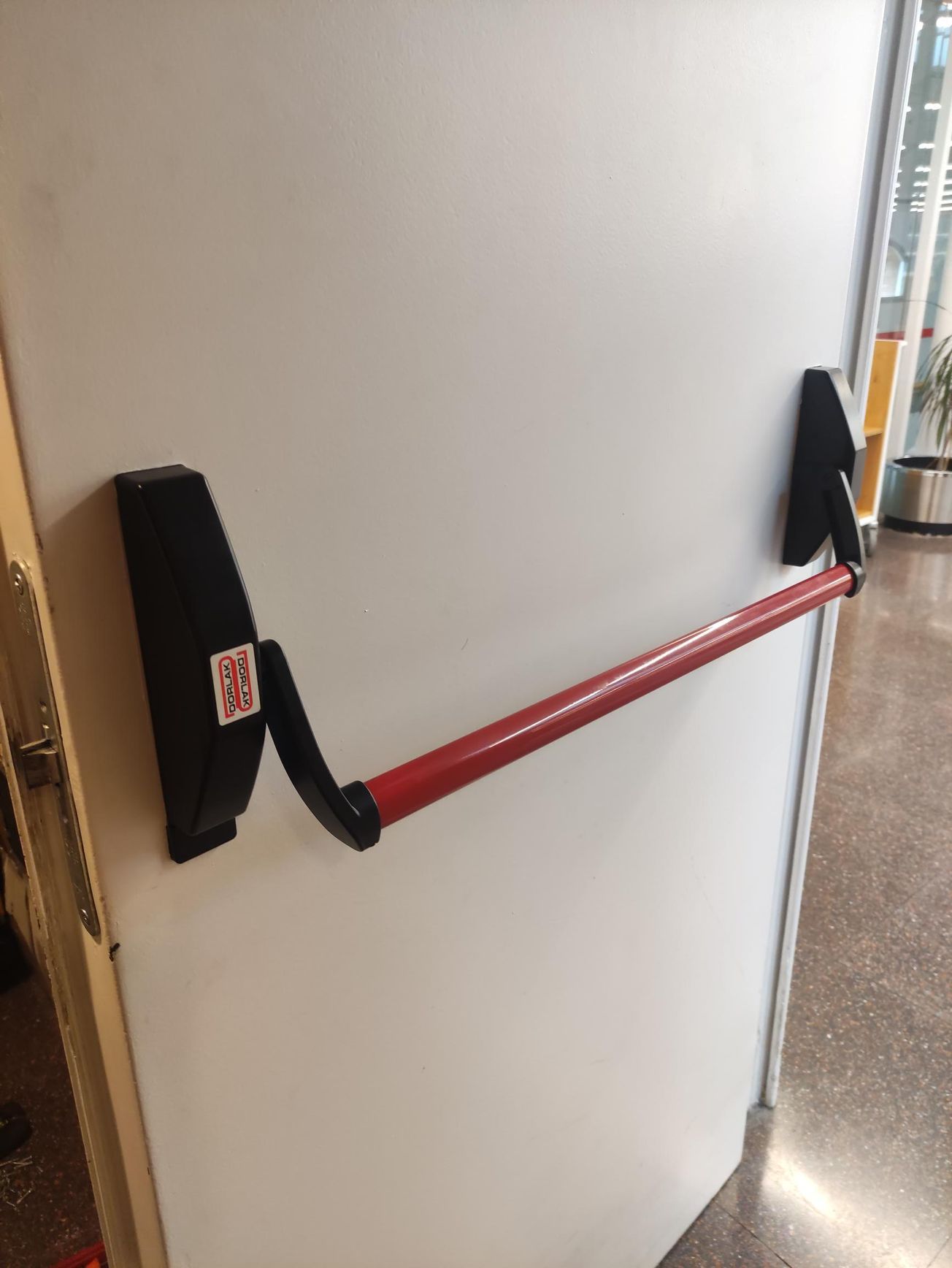 Una puerta blanca con una barra antipánico roja.