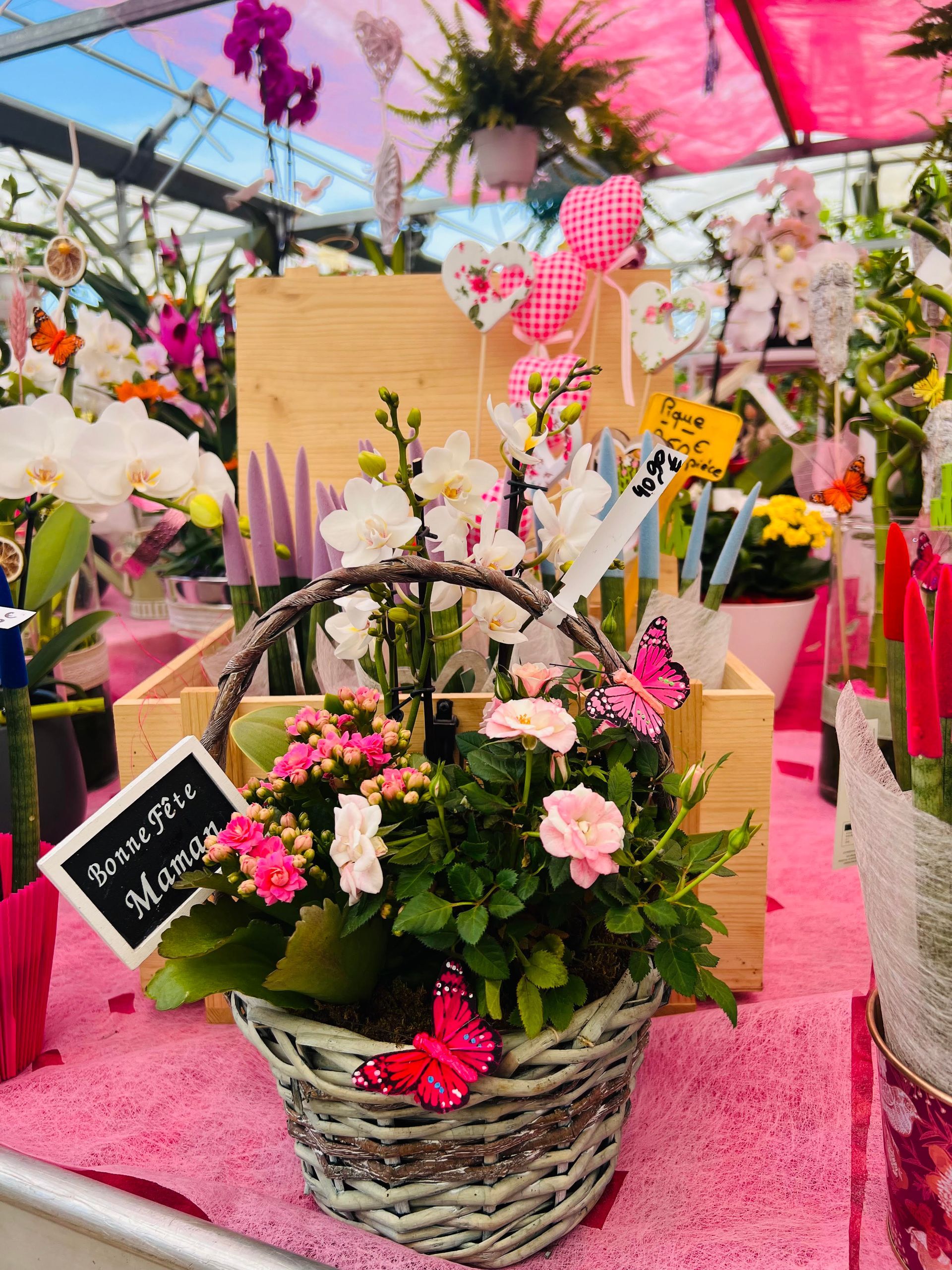 Composition florale dans un panier avec des roses miniatures et un message 'Bonne fête Maman', ornée de papillons et de décorations.