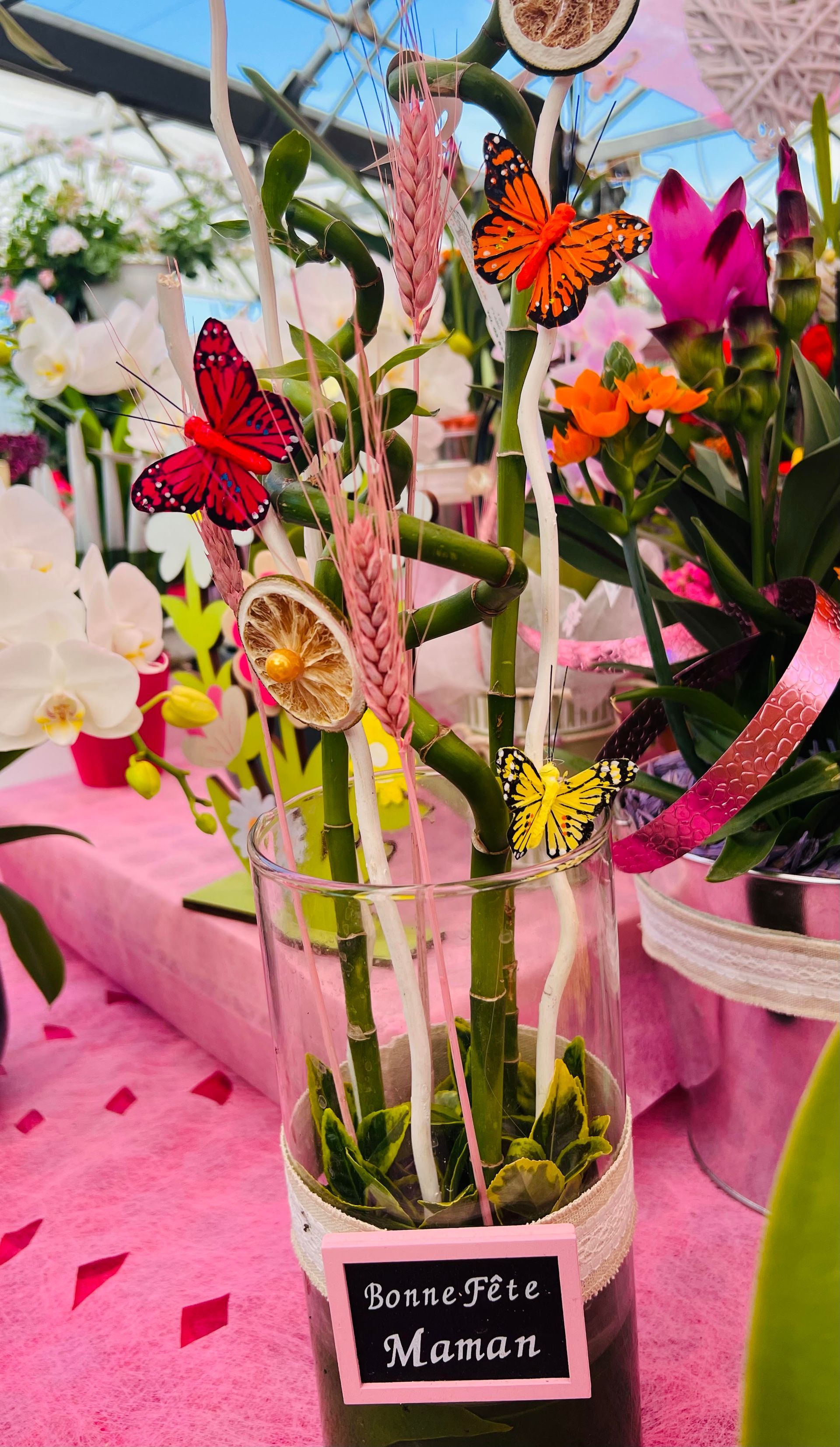 Orchidées élégantes dans un vase décoré de papillons rouges et jaunes, parfaites pour une touche florale raffinée.