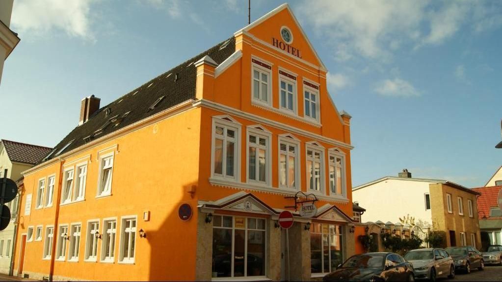 Leuchtend orangefarbenes Gebäude mit weißen Verzierungen, HOTEL-Schild, Straße und geparkten Autos.