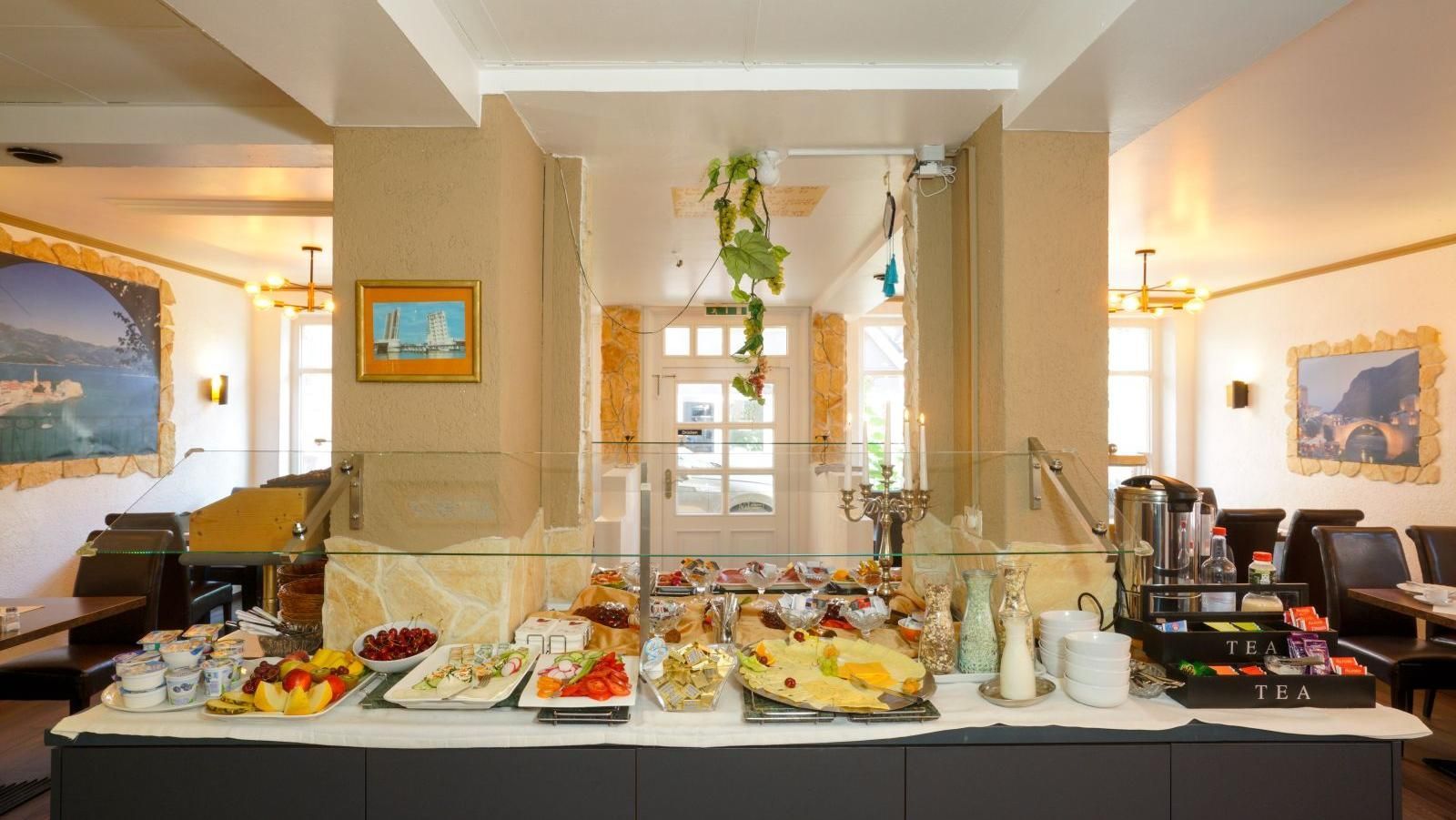 Frühstücksbuffet im Speisesaal eines Hotels mit Speisenauslage, Kaffee und Sitzgelegenheiten.