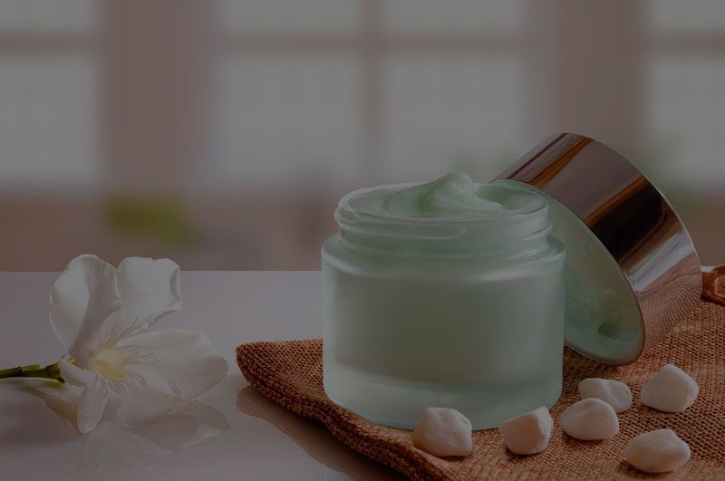 Un tarro de crema está sobre una mesa al lado de una flor.