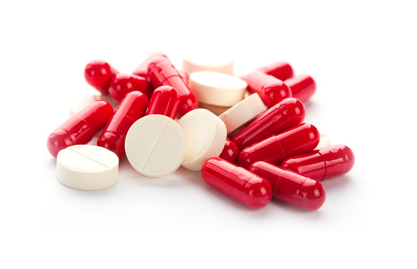 Una pila de pastillas y cápsulas rojas y blancas sobre un fondo blanco.