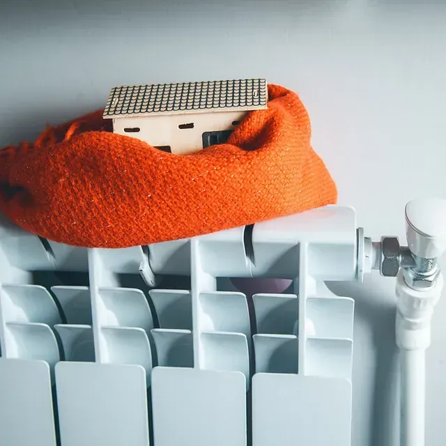 Una pequeña casa está sentada encima de una bufanda naranja sobre un radiador.
