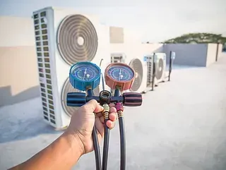 Una persona sostiene un par de medidores frente a un acondicionador de aire.