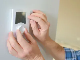 Una persona está ajustando un termostato en una pared.