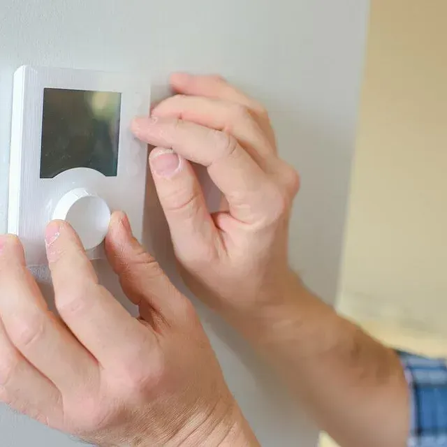 Una persona está ajustando un termostato en una pared.