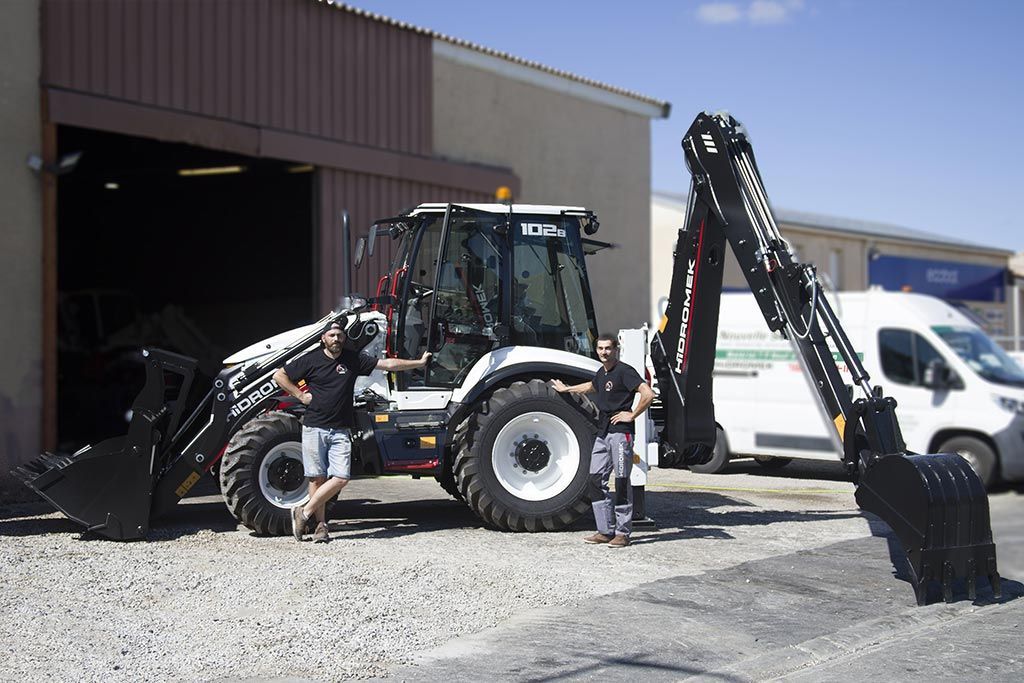 Tracteur Hidromek avec godets avant et arrière et deux employés d'AMAT TP