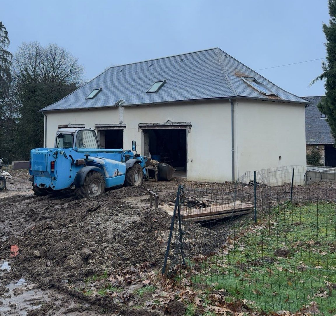 Engin de terrassement bleu devant une maison blanche.
