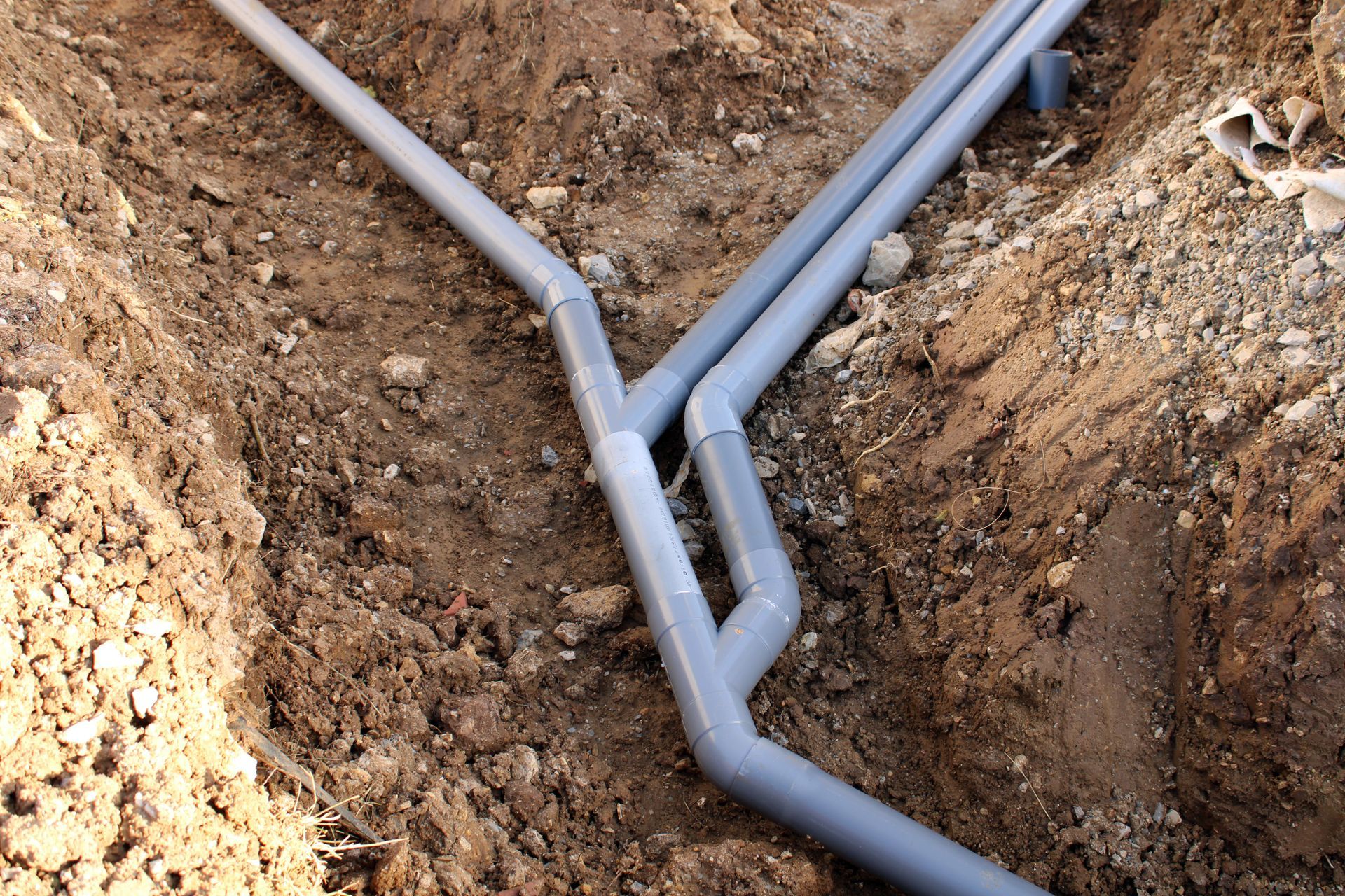Des tuyaux en PVC gris dans une tranchée de terre.