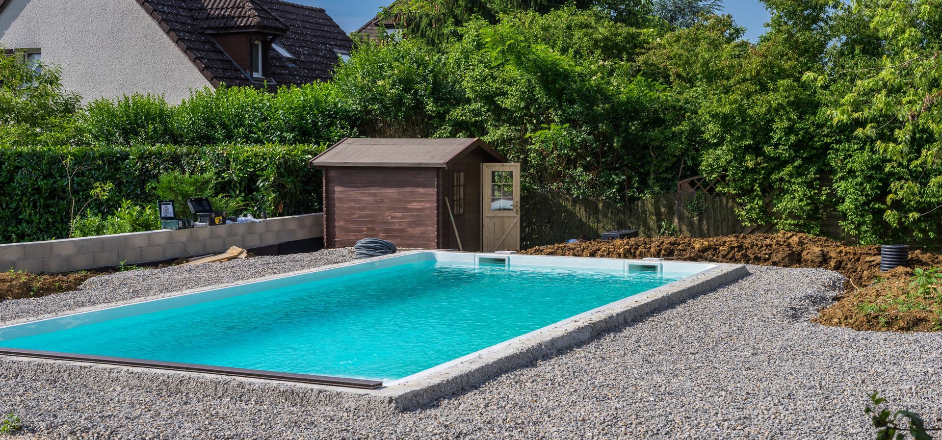 Piscine rectangulaire dans un jardin gravillonné avec un petit pavillon de piscine.