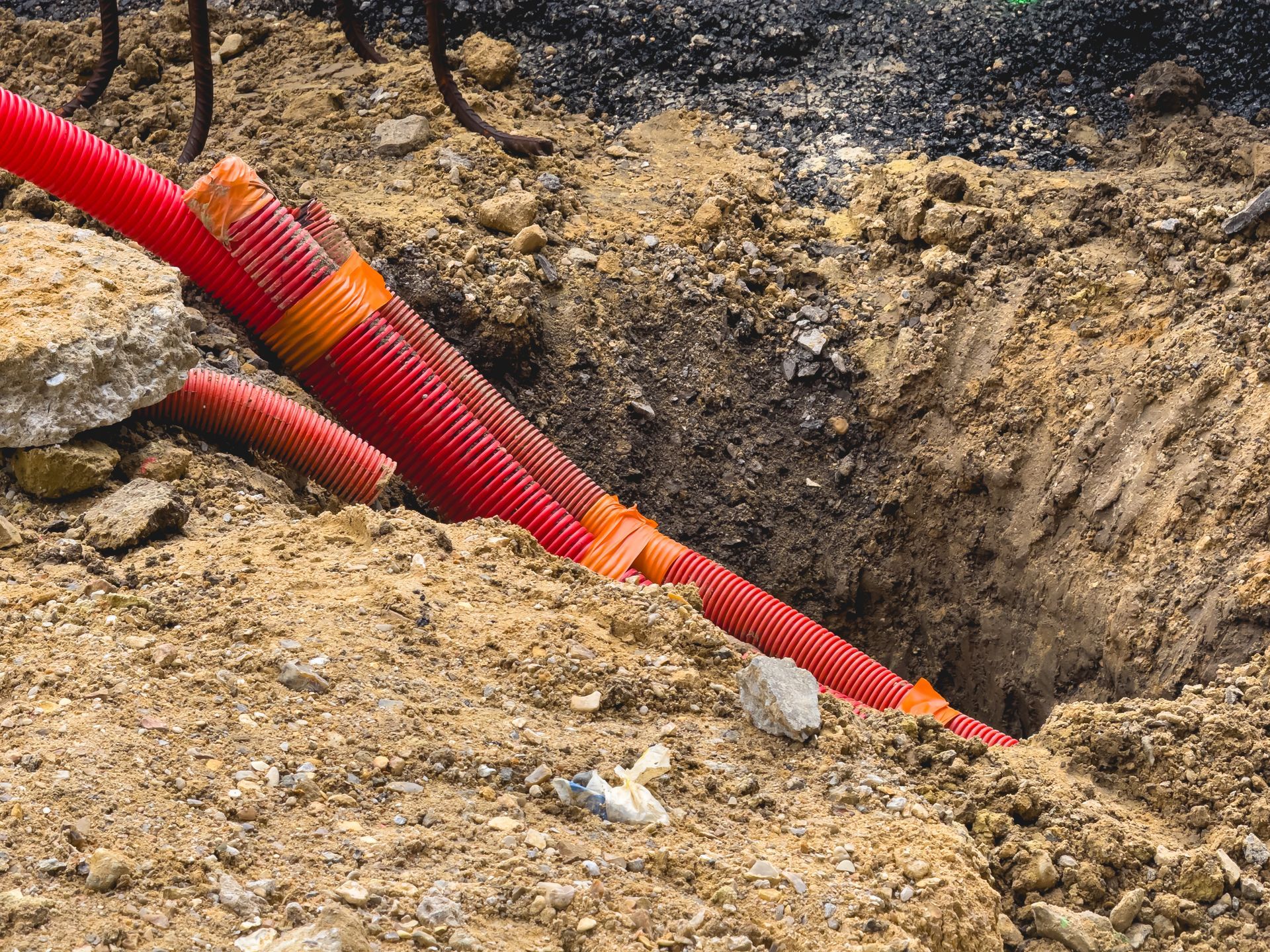 Des tuyaux de service rouges sont posés dans une tranchée de terre sur un chantier de construction.