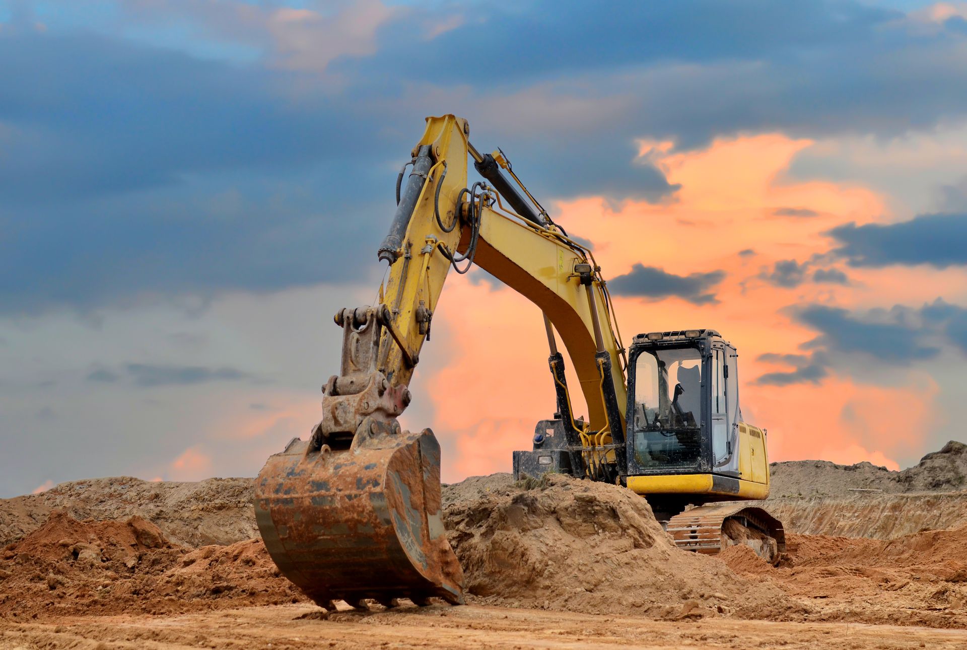 Une pelleteuse jaune creuse le sol sur un chantier de construction sous un ciel nuageux.