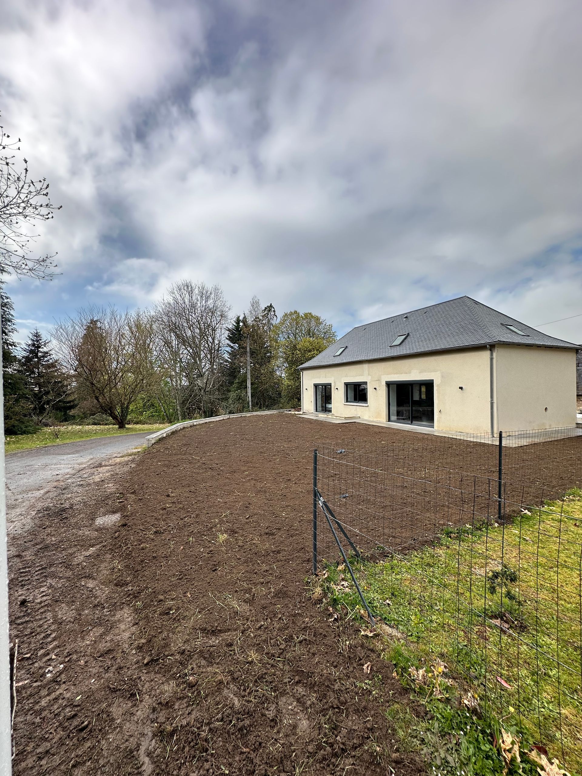 Maison neuve au toit gris, bordée d'une allée de gravier et d'un jardin.