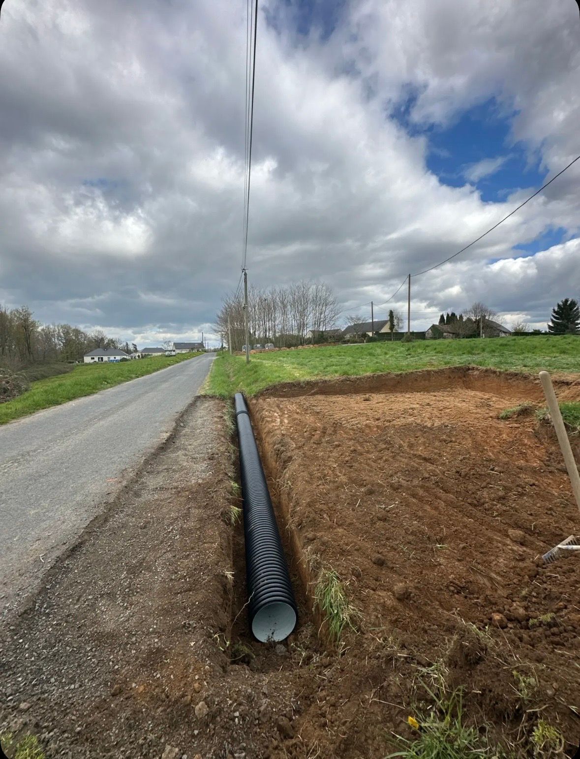 Bord de route rurale avec un tuyau de drainage noir sous un talus de terre.