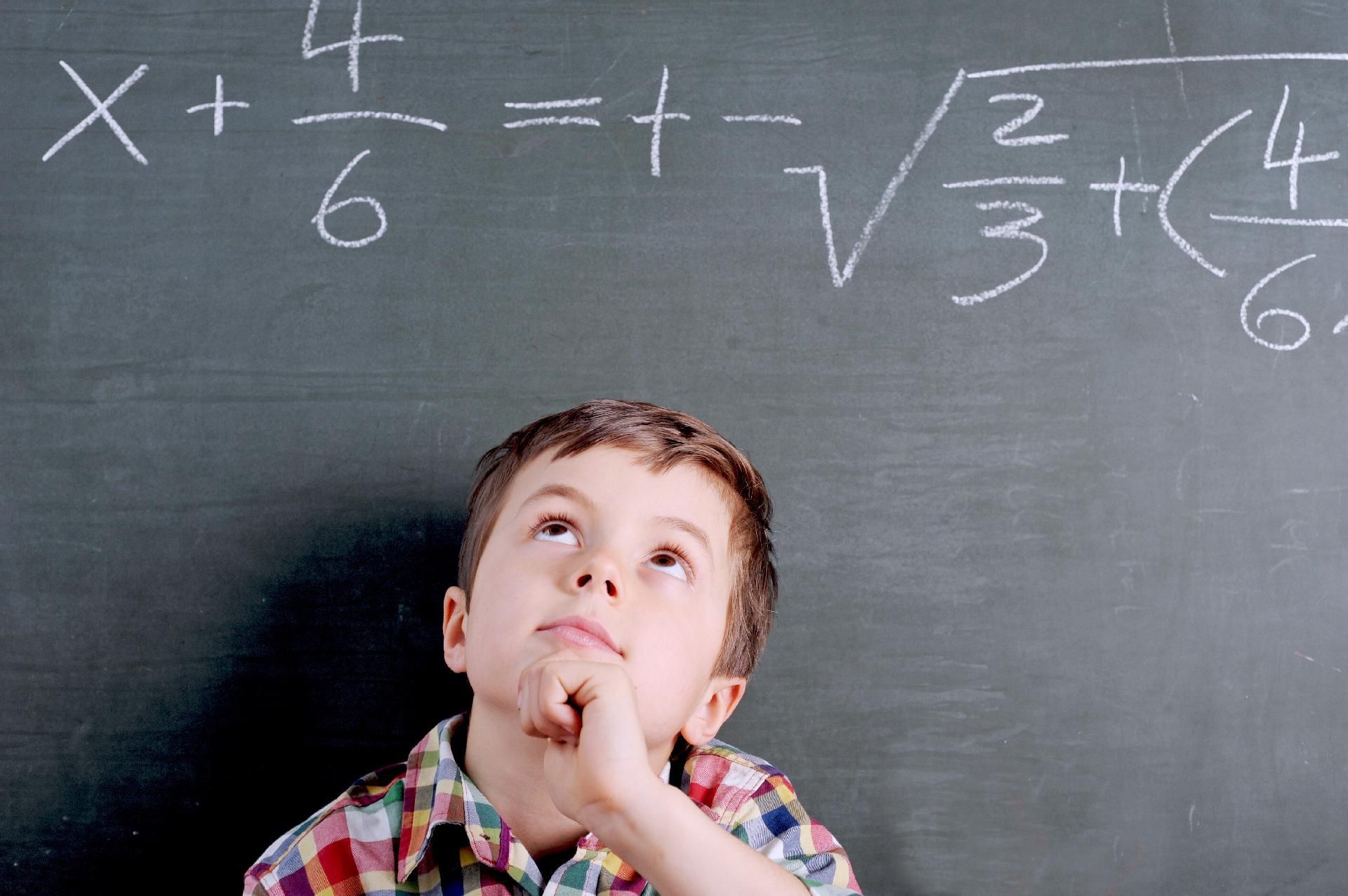 Junges Kind blickt nachdenklich auf eine Schultafel mit mathematischen Formeln.