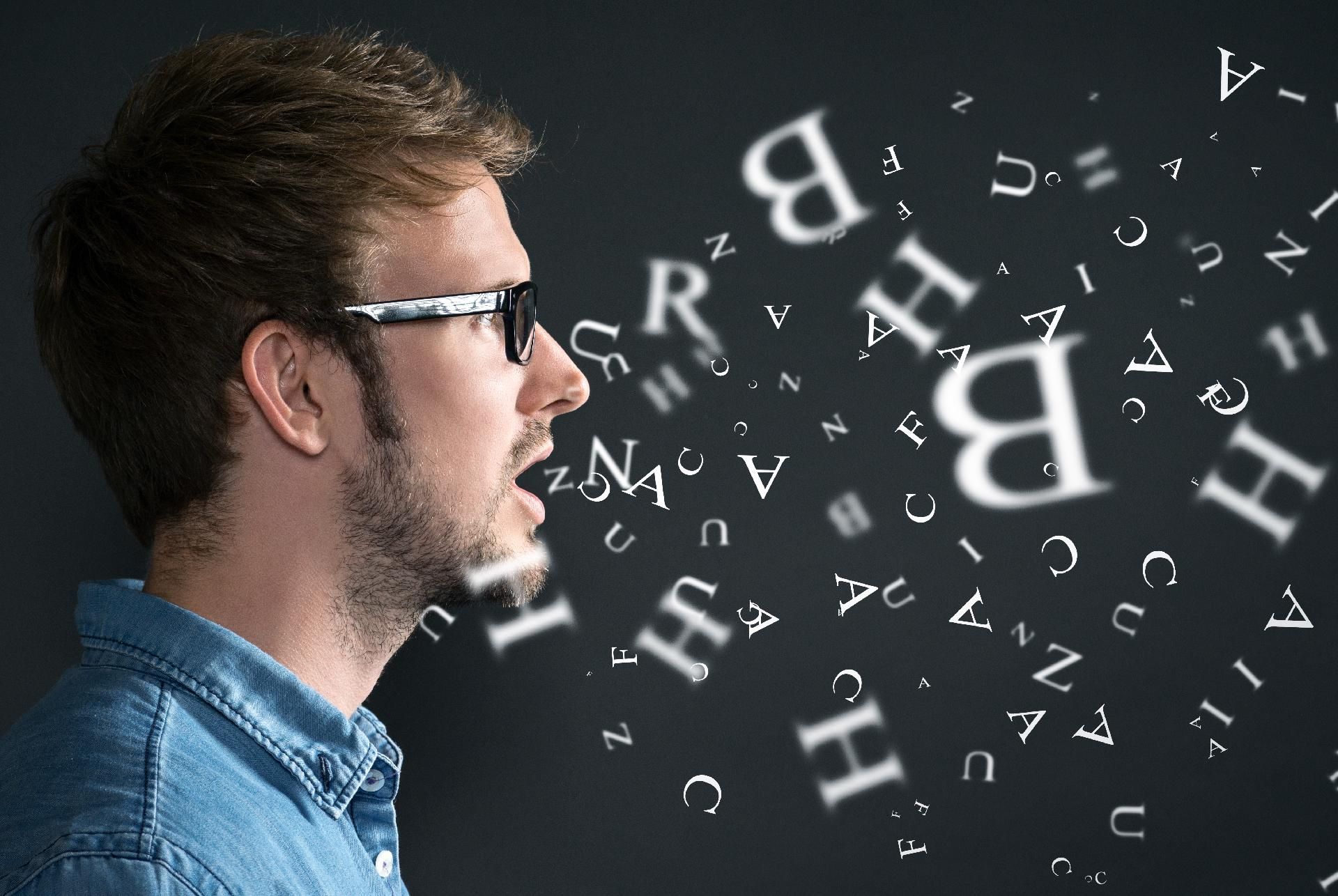Mann im Profil mit fliegenden Buchstaben und Symbolen vor dunklem Hintergrund.