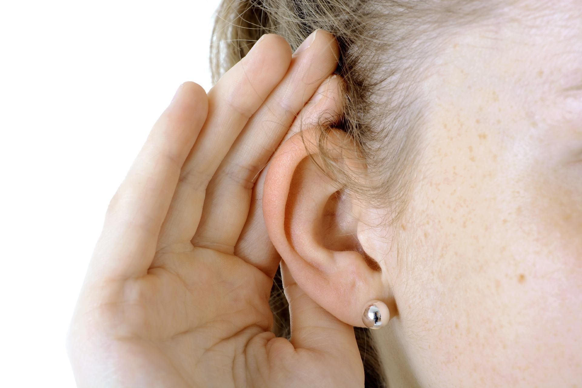 Nahaufnahme eines Ohrs, eine Hand ist zum besseren Zuhören dahinter gehalten.