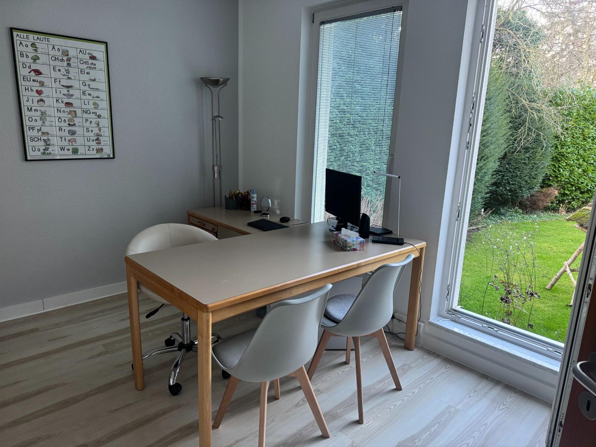 Behandlungsraum mit Tisch und Stühlen neben einem Fenster mit Blick ins Grüne.