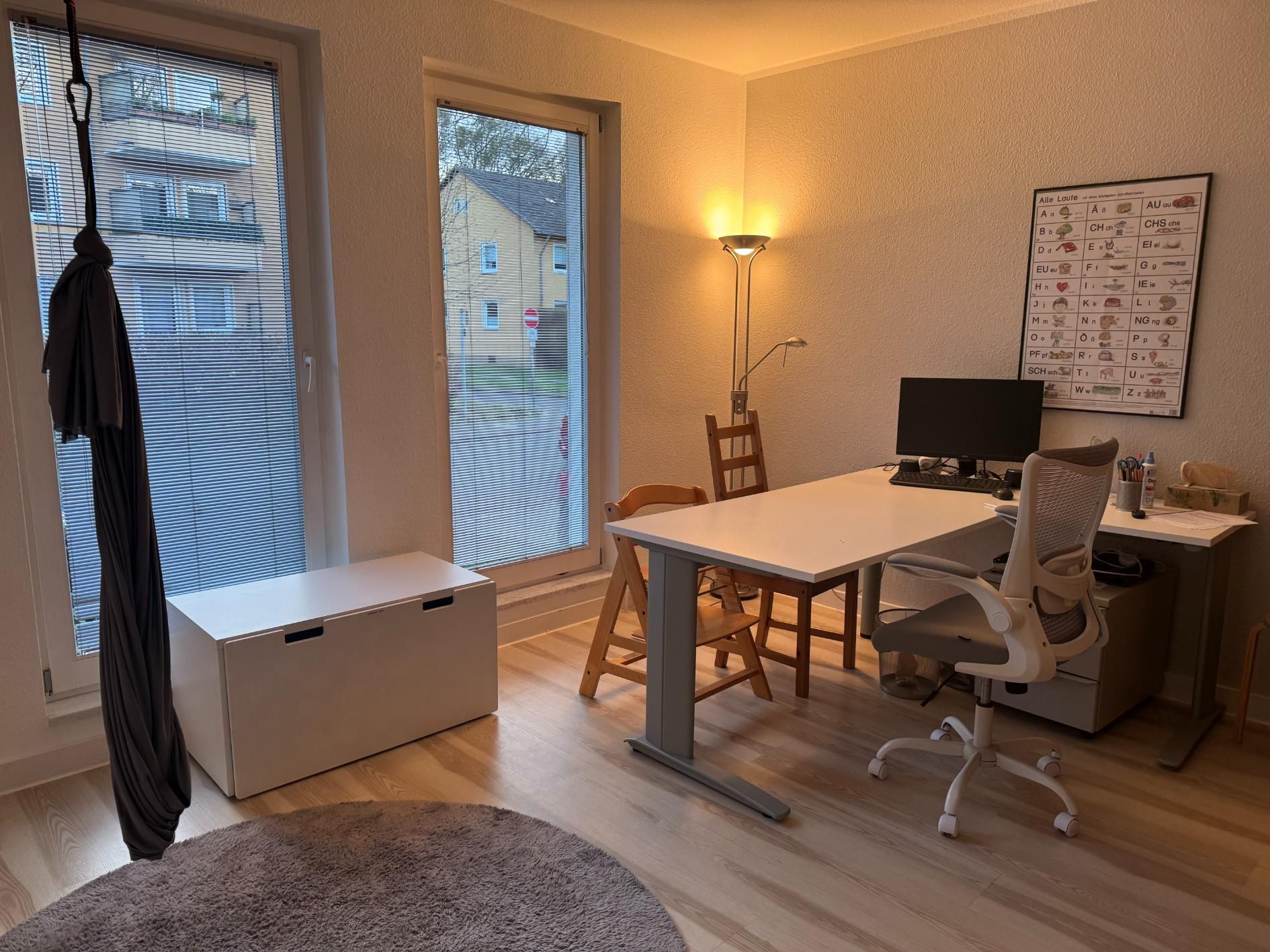 Büro mit Schreibtisch, Stühlen, Stehlampe und Fenster.