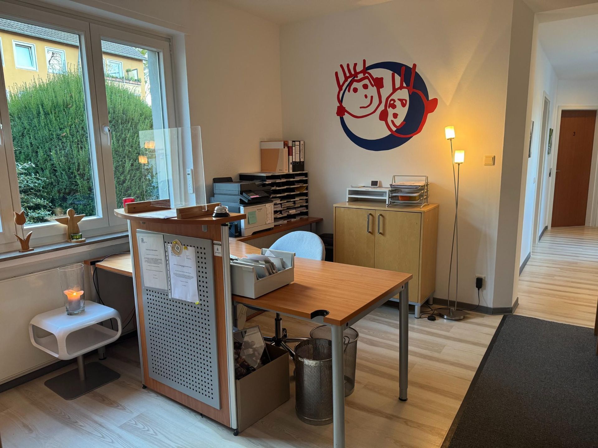 Heller Arbeitsraum mit Tisch, Stühlen, Regal und Fensterfront.