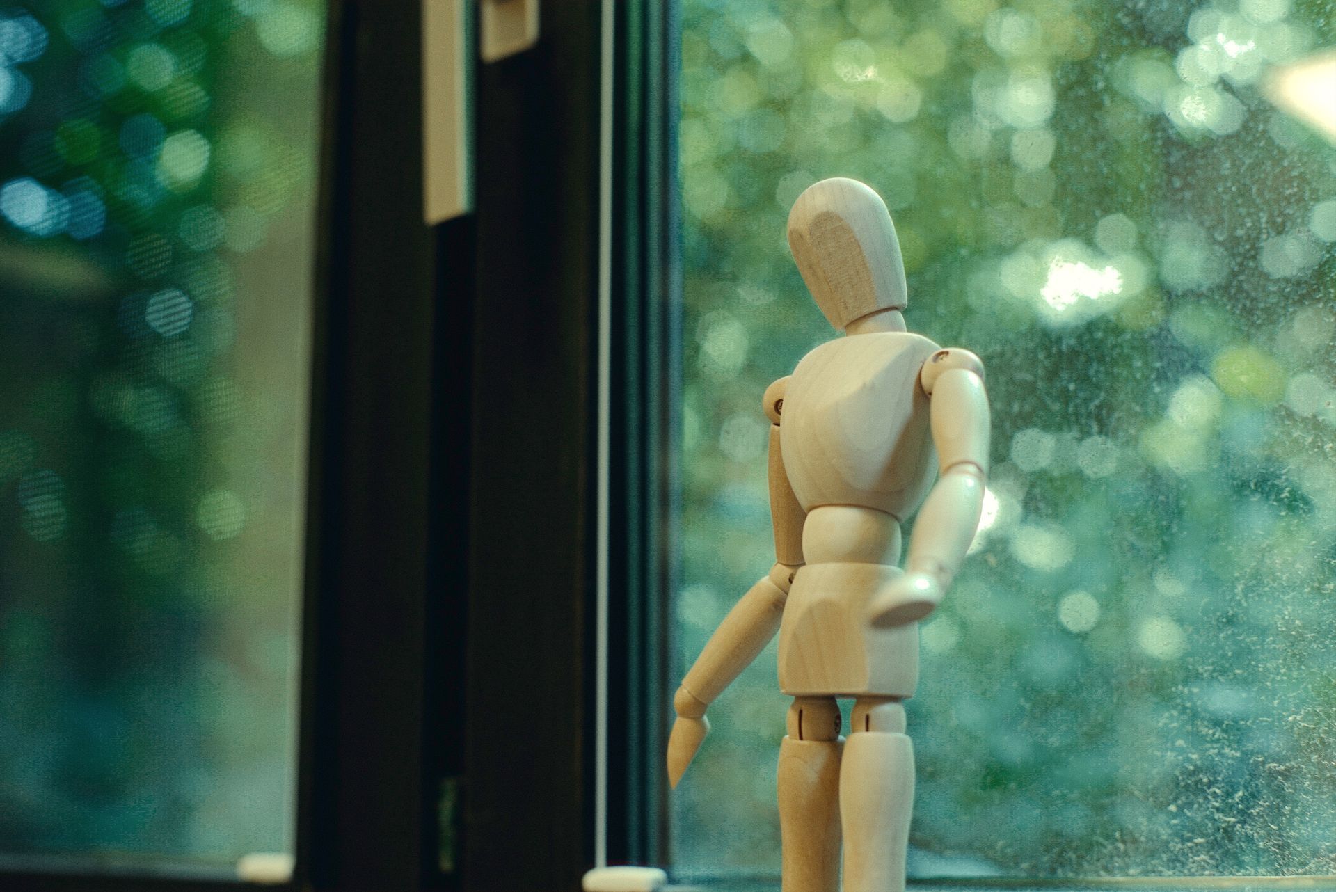 Eine hölzerne Schaufensterpuppe steht vor einem Fenster.