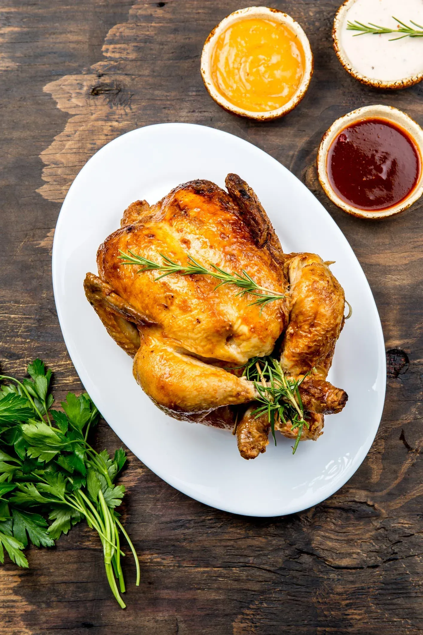 Un pollo asado está en un plato blanco sobre una mesa de madera.