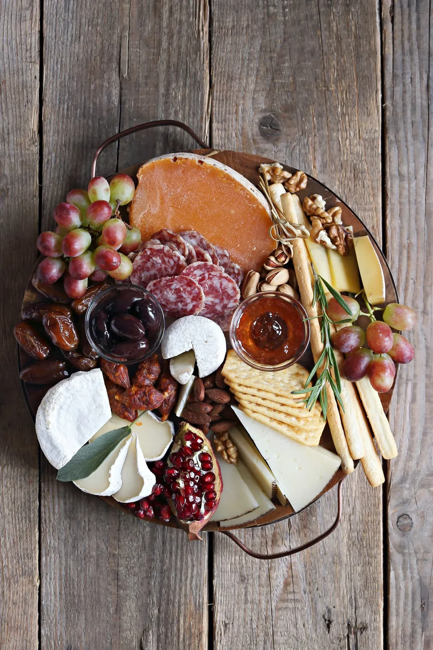 Una tabla de cortar de madera cubierta con una variedad de quesos, carnes, nueces y uvas.