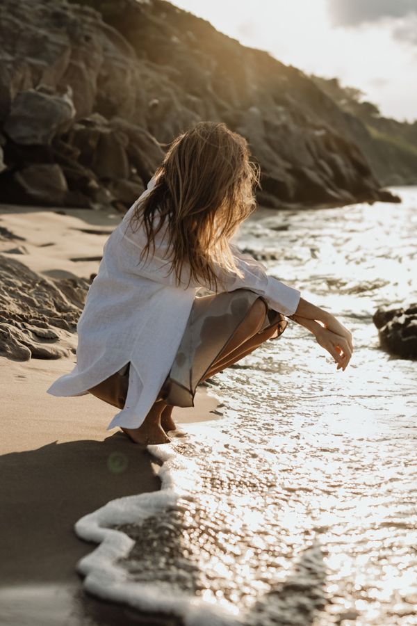 Une femme en bikini noir se tient sur une plage, posant avec des vagues en arrière-plan.