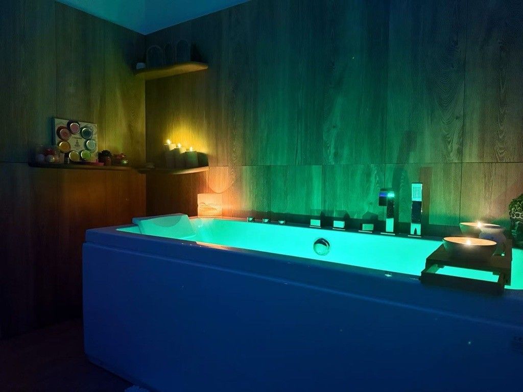 Jacuzzi dans un spa faiblement éclairé, éclairé de lumières roses et oranges, avec des bougies.