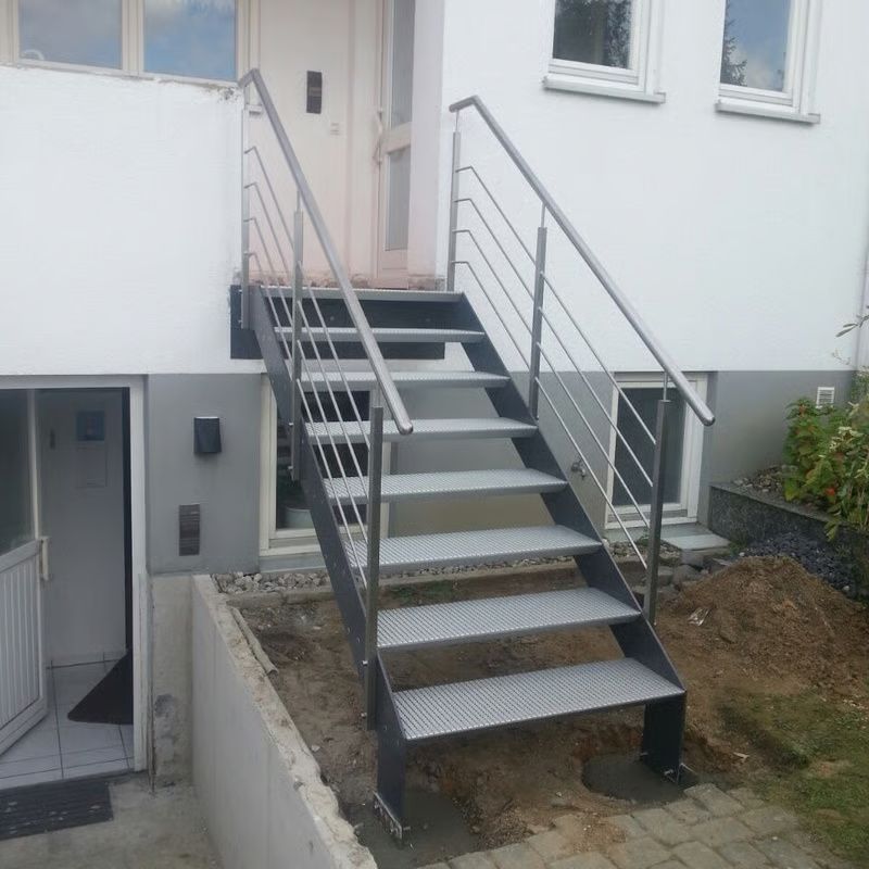 Eine Außentreppe aus Metall mit Geländer führt zu einer Tür neben einem weißen Haus.