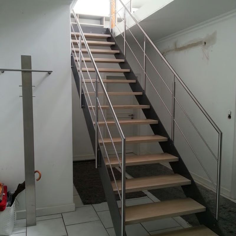 Metalltreppe im Innenbereich mit Holzstufen, Handläufen und Fliesenboden in einem weißen Raum