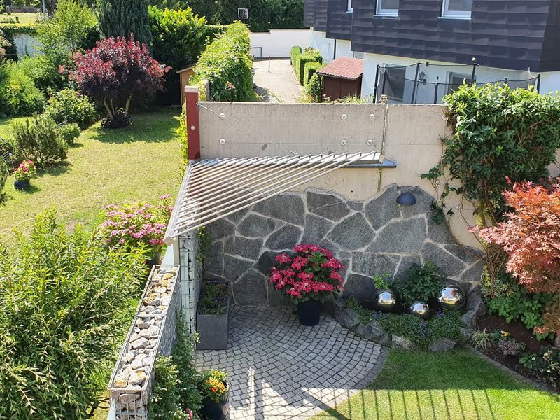 Hinterhofgarten mit Steinmauer, blühenden Pflanzen und gepflasterter Terrasse im hellen Sonnenlicht