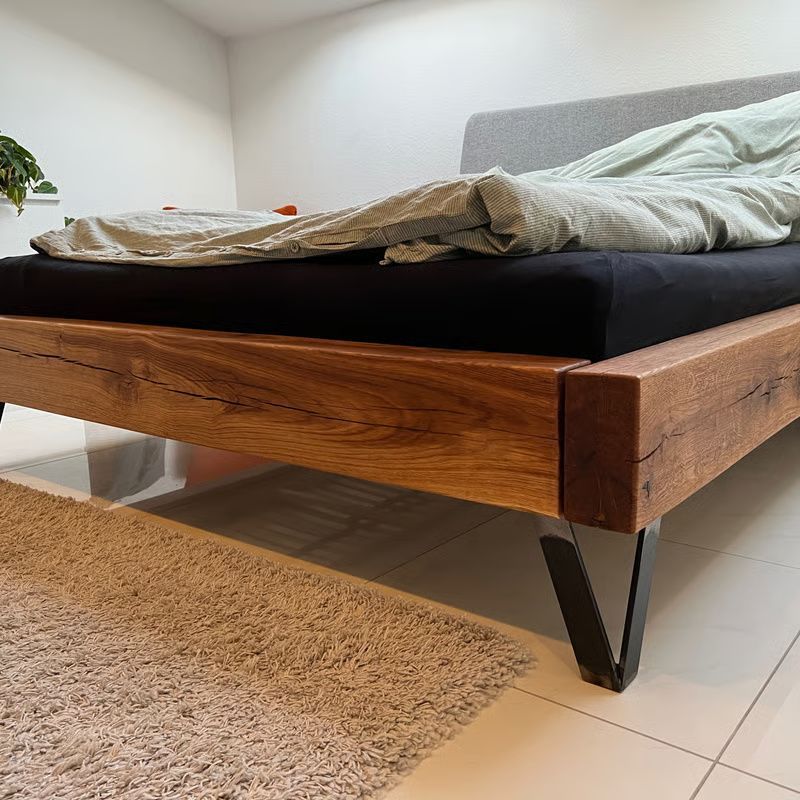 Modernes Holzbett mit schwarzen Beinen, Bettwäsche und ein beiger Teppich in einem hellen Schlafzimmer