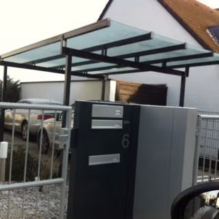 Moderner Hauseingang mit schwarz-grauem Tor und überdachtem Carport, hinter dem Zaun steht ein Auto.
