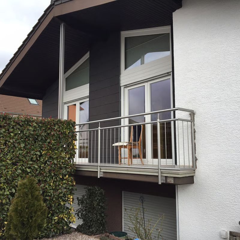 Moderner Hausbalkon mit Glastüren, zwei Holzstühlen und einer Hecke davor