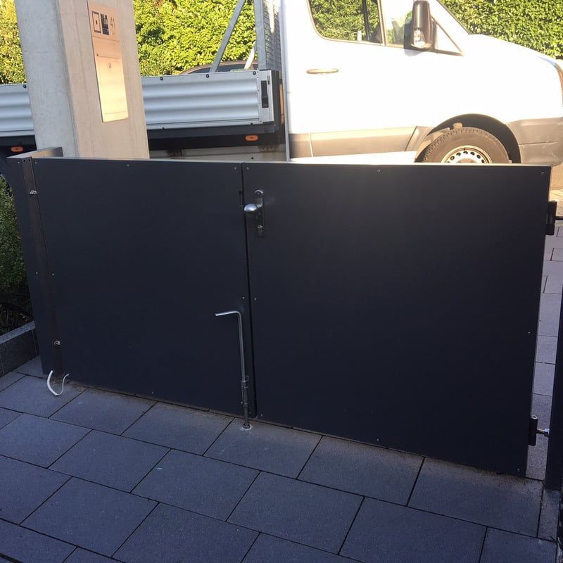 Ein schwarzes Metalltor versperrt eine Einfahrt; dahinter parkt ein weißer Lieferwagen.
