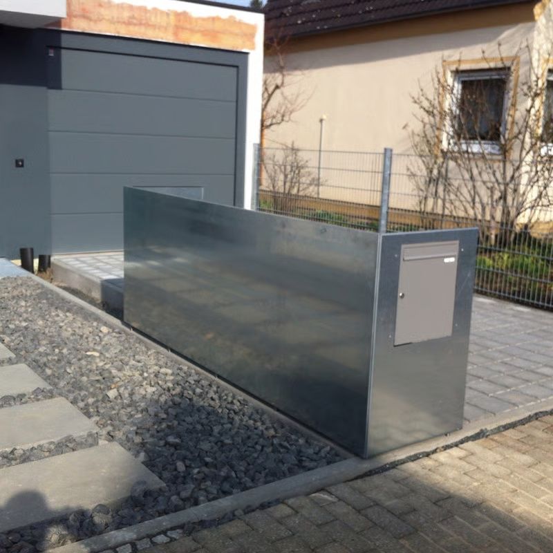 Modernes graues Metall-Einfahrtstor neben einer Garage und einem gepflasterten Gehweg in einem Wohngarten