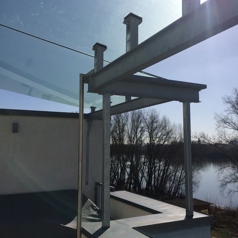 Pergola-Gerüst auf dem Dach neben einem See, im Hintergrund strahlender Sonnenschein und kahle Bäume.