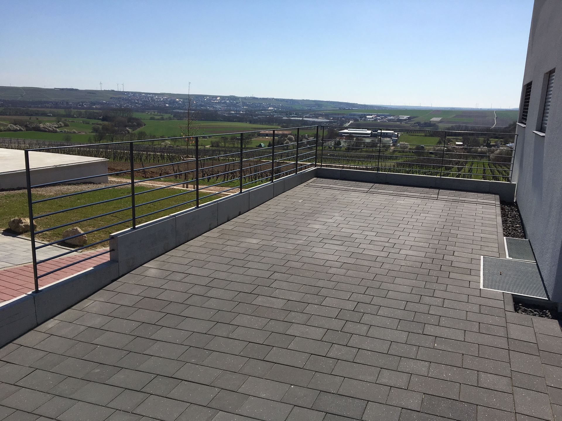 Dachterrasse mit grauen Pflastersteinen, Glasgeländer und Stadtblick in der Ferne