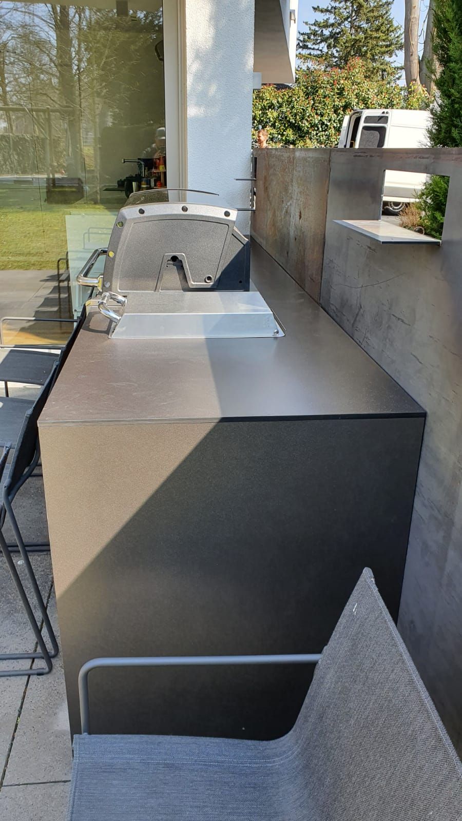 Außenterrasse mit in eine graue Betonarbeitsplatte neben Glastüren eingelassenem Edelstahlgrill.