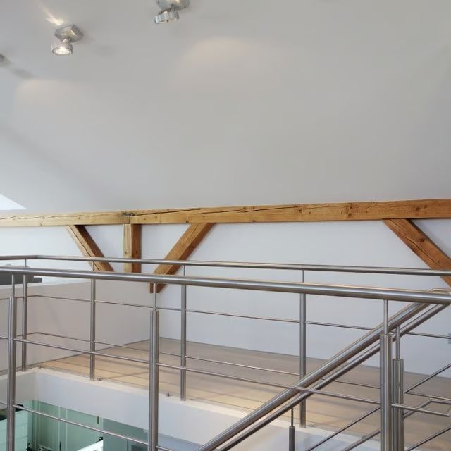 Modernes Loft-Interieur mit weißen Wänden, sichtbaren Holzbalken und einem Balkongeländer aus Metall.