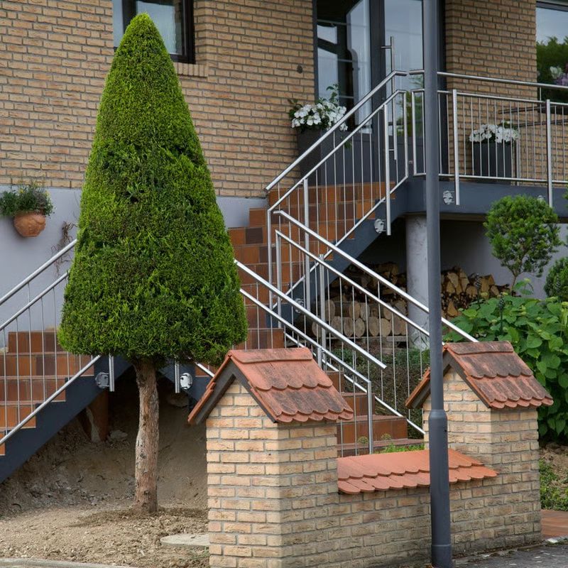 Fassade aus Backstein mit Metalltreppe, beschnittenem Kegelbaum und kleinen Nebengebäuden aus Backstein