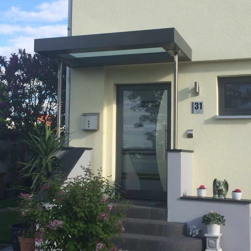 Vordereingang eines Hauses mit dunkler Markise, Glastür, Treppe und Topfpflanzen
